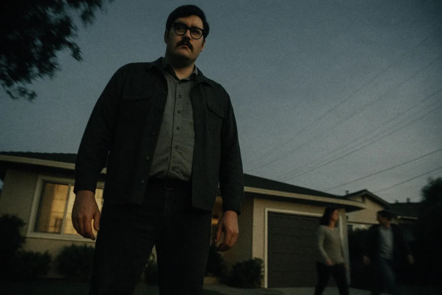 En skikkelse, der ligner Edmund Kemper, står udenfor et forstadshus i Californien, truende høj med et tomt blik, mens naboer går forbi uvidende, hvilket symboliserer de skjulte rædsler, der lurer under overfladen.